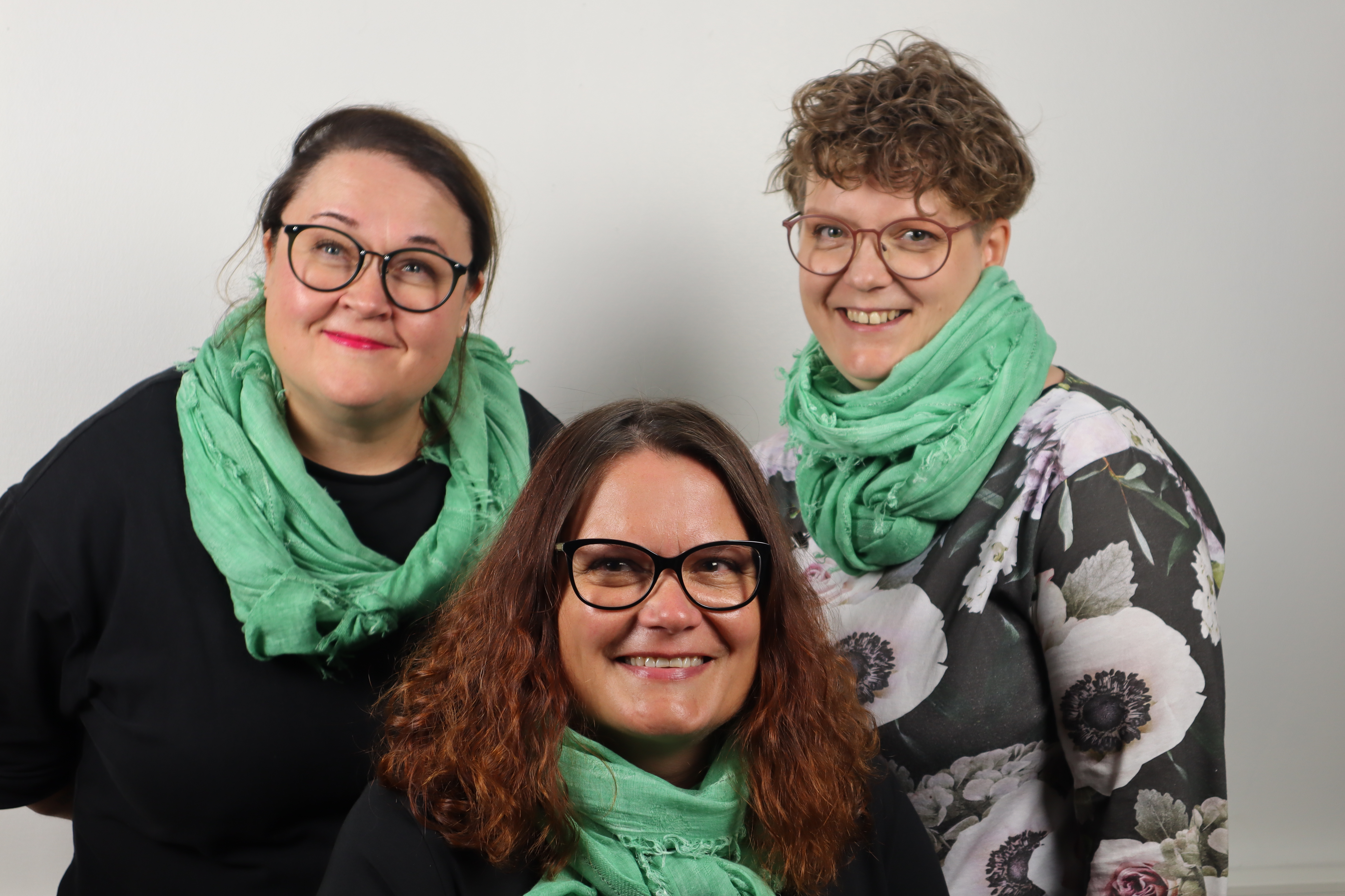 Kolme naista , yksi istuu edessä ja kaksi seisoo takana hymyilevät kameralle